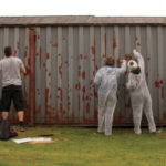 A group of people wearing white overalls paint a metal storage container
