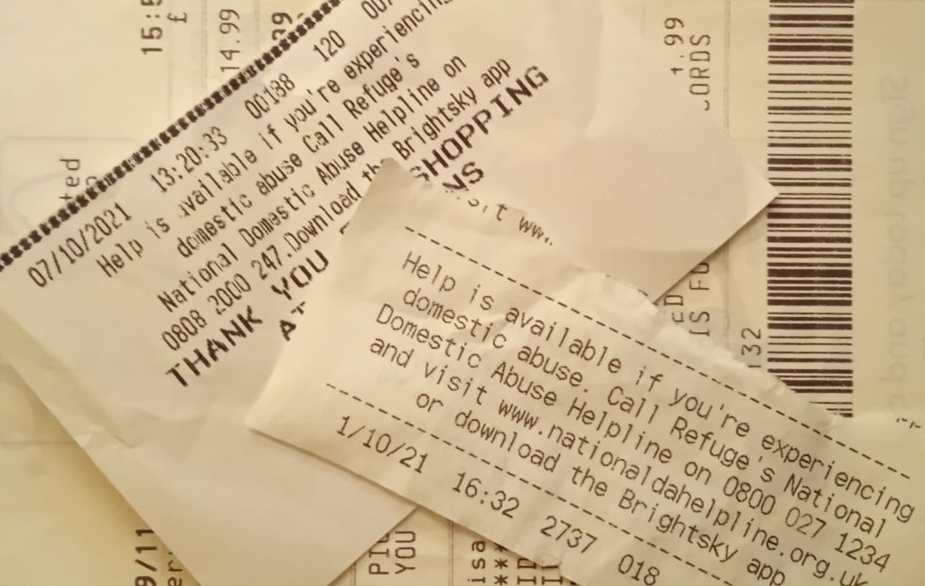 Photograph of the bottom of supermarket receipts featuring helplines for domestic abuse.