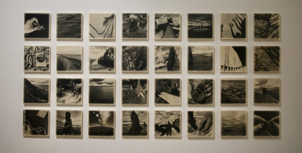 A grid of 24 black and white photographs are displayed on a while wall.